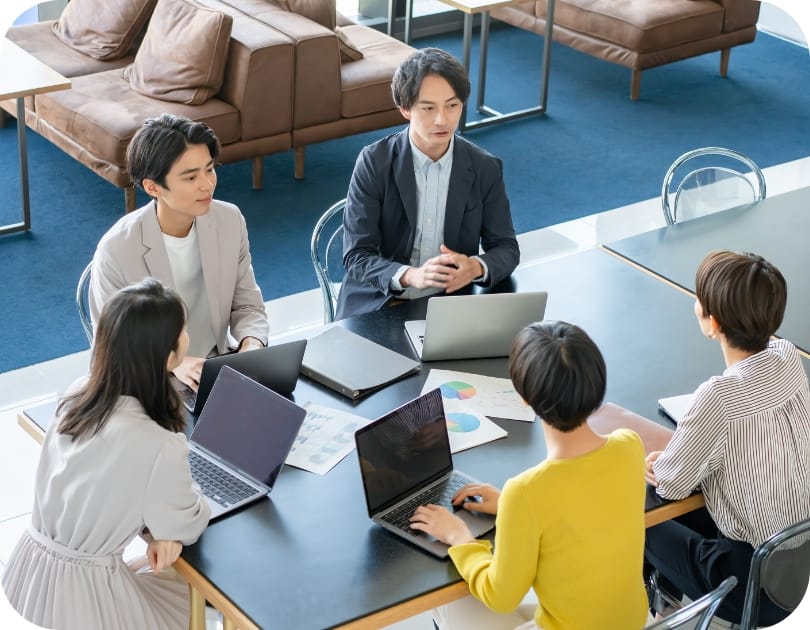 会議室で5人の若手ビジネスパーソンがパソコンを使いながら打ち合わせ中