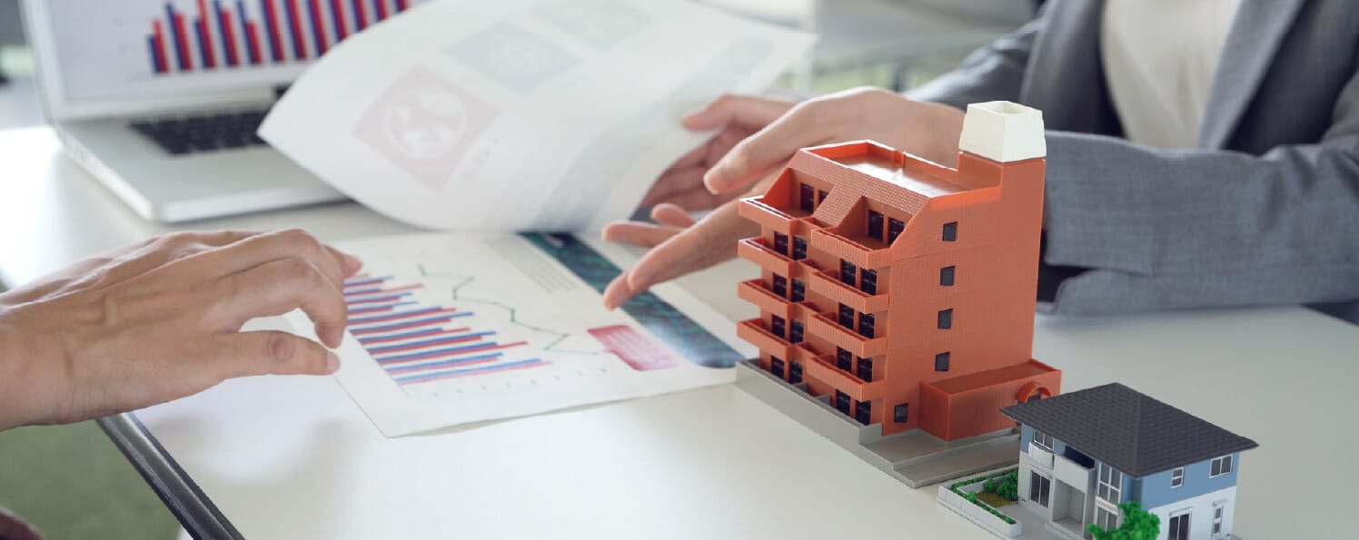 マンションと戸建ての模型を机に置き、資料を見ながら不動産に関する説明をする様子