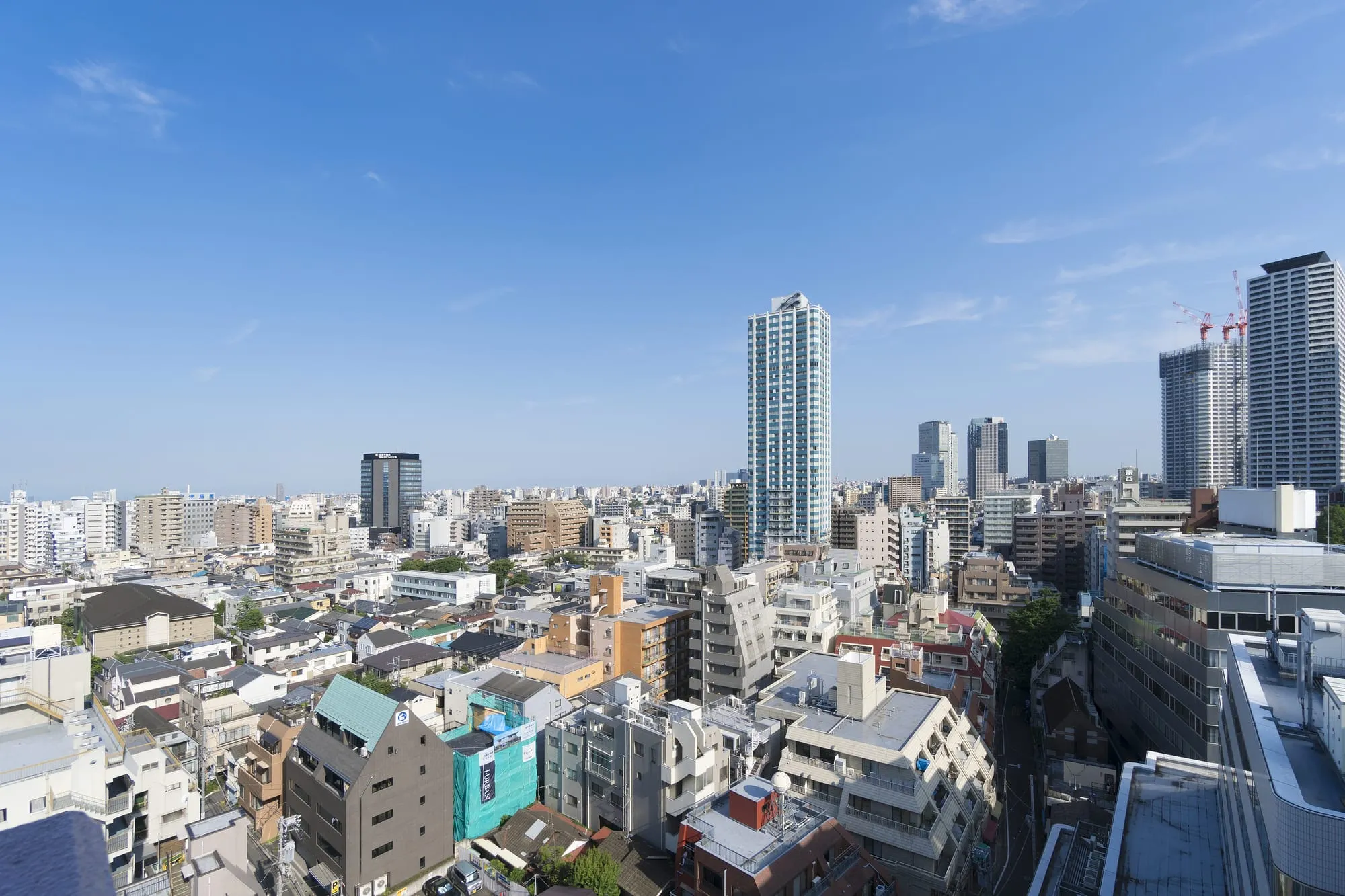 中高層ビルと住宅が混在する都市の風景で、晴天のもとに建物が密集している様子を俯瞰で撮影