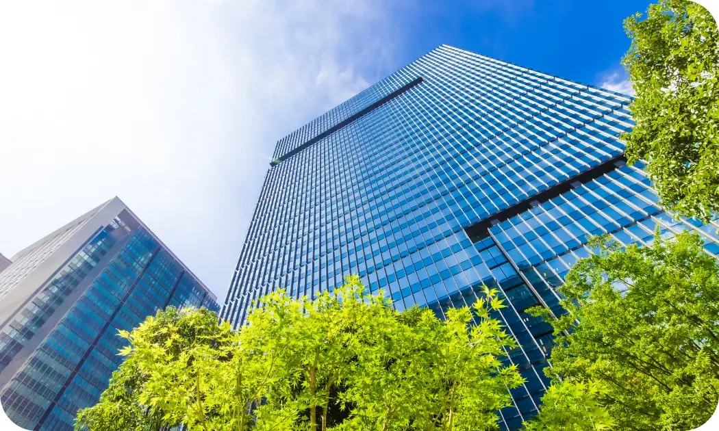 青空の下、ガラス張りの高層ビルを下から見上げたダイナミックな構図